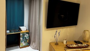 A room with a TV mounted on the wall, a wooden side table with a vase and a tray of oysters, and a desk with a printer and a plant. - Small vacation villa, beach and barbecue :-) (Bastelicaccia)