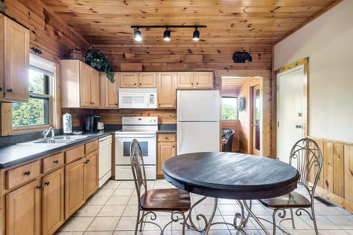 A kitchen with wooden cabinets, a microwave, a refrigerator, a stove, and a round table with chairs.