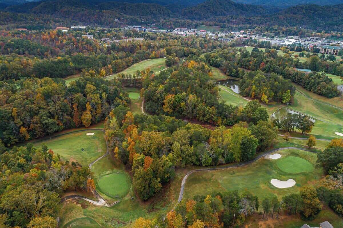 Une vue aérienne d’un terrain de golf entouré d’un feuillage automnal et de bâtiments résidentiels.