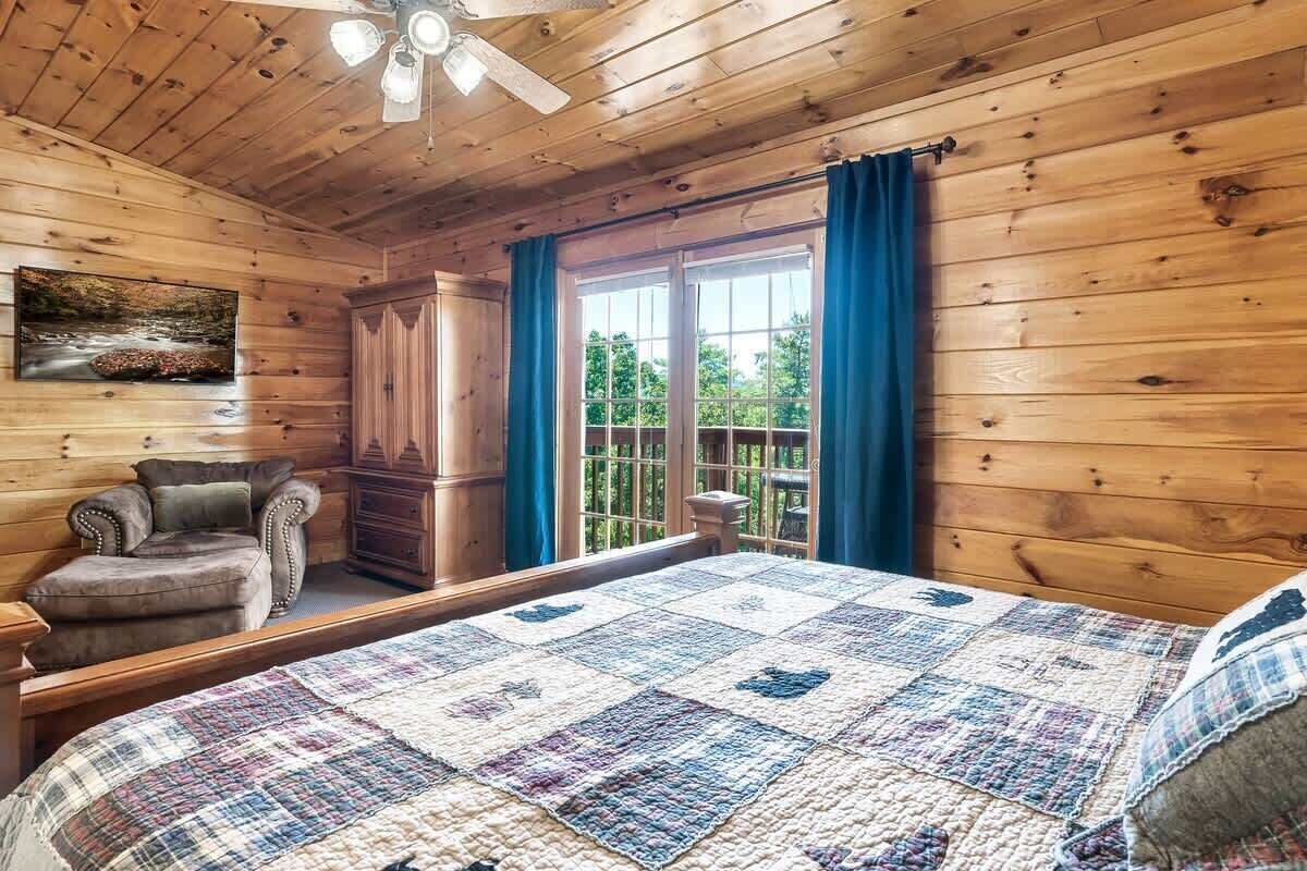 A wooden cabin bedroom with a bed, a chair, a dresser, and a window with curtains.