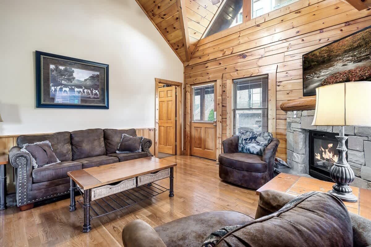 A cozy living room with a wooden ceiling, a fireplace, and a large window.