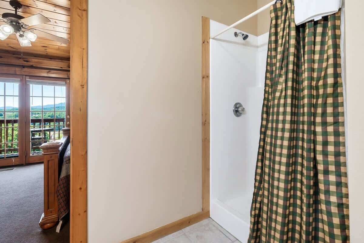 A room with a wooden ceiling, a shower with a checkered curtain, and a view through a glass door.