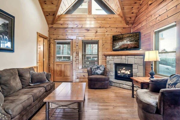 A log cabin interior with a fireplace, wooden walls, a sofa, and a dining table.