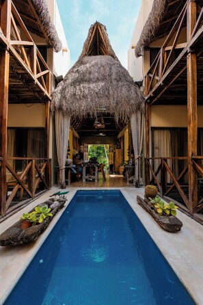A pool area with a thatched roof structure, wooden railings, and potted plants. - Alma de Zorro (Bacalar)