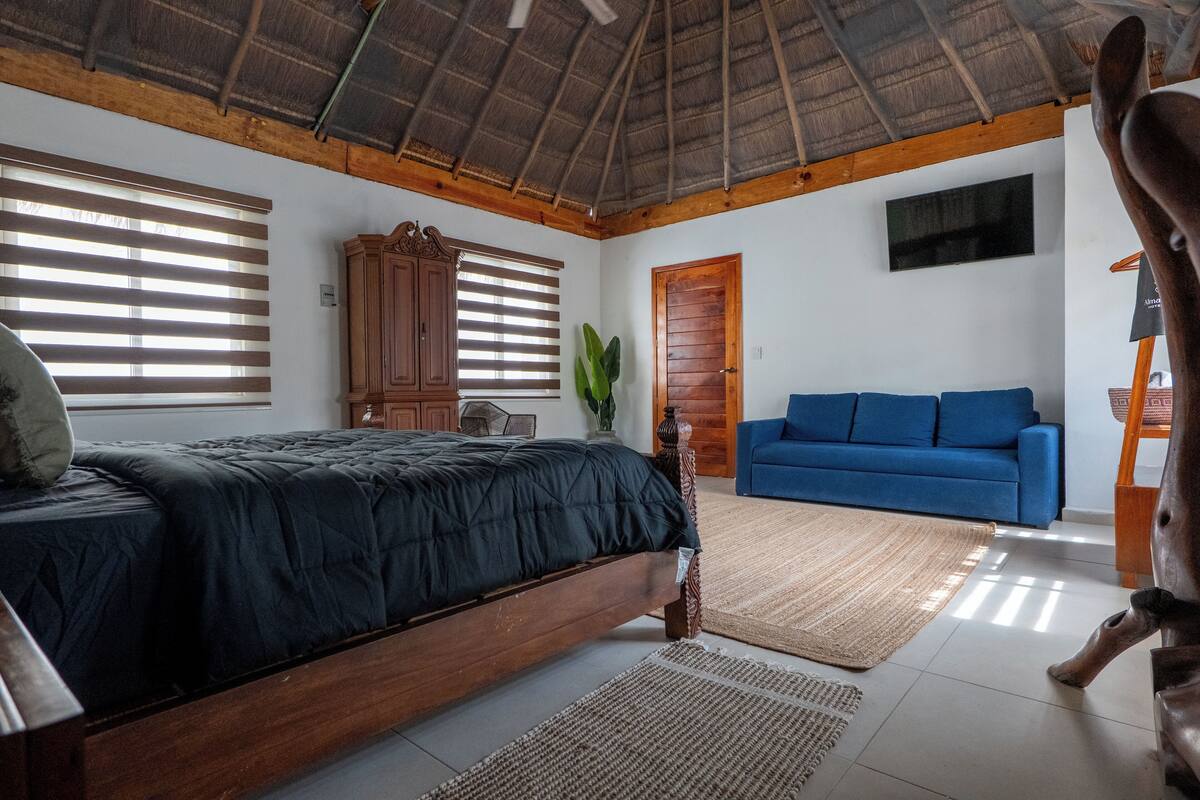 A bedroom with a bed, a blue sofa, wooden furniture, and a large plant.