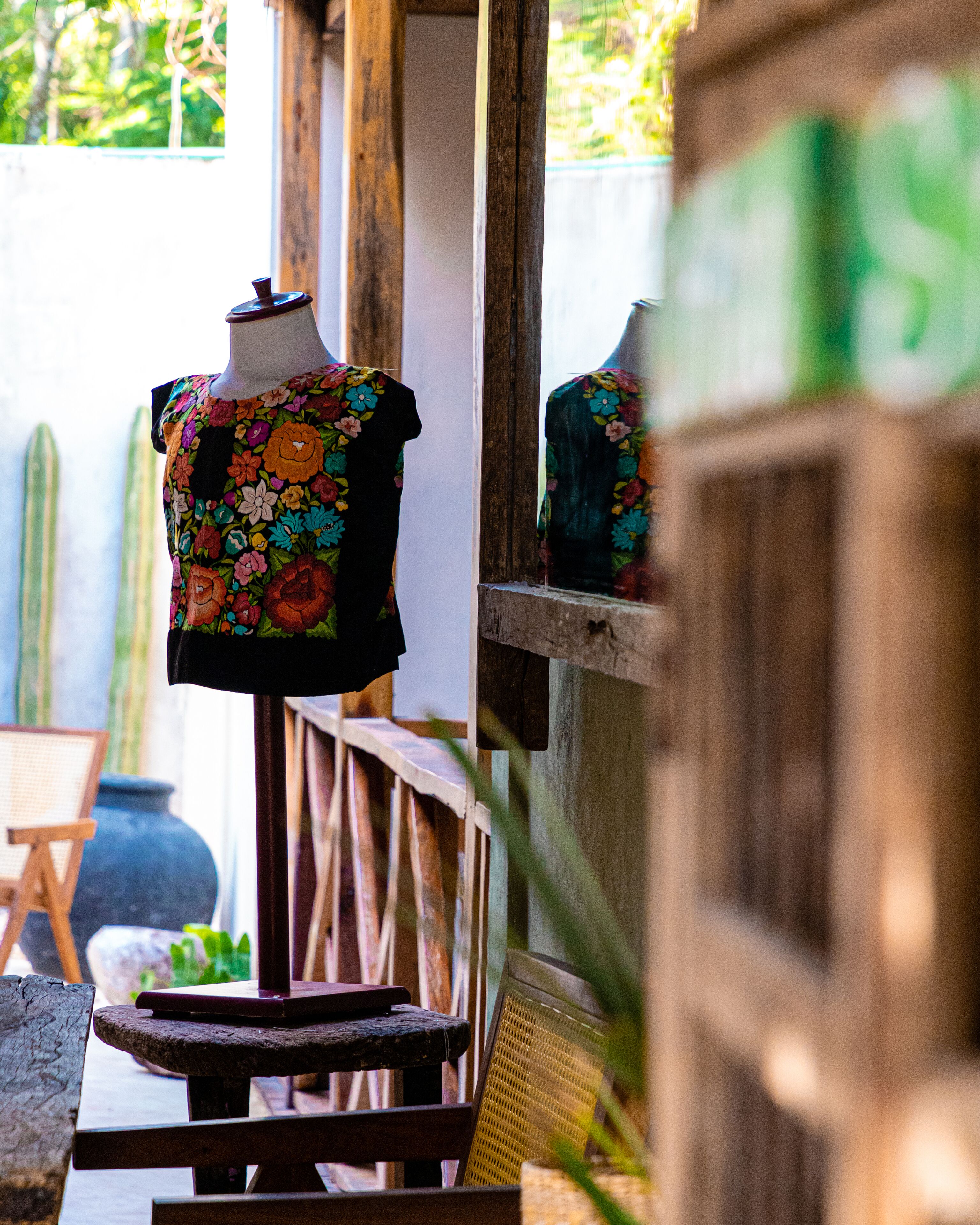 Un mannequin portant une robe à motifs floraux, placé dans un décor extérieur avec une structure en bois et un cactus en arrière-plan.