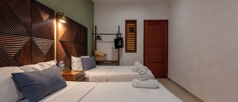 A hotel room with two beds, wooden headboards, a bedside table with a lamp, a wardrobe, and a television mounted on the wall.