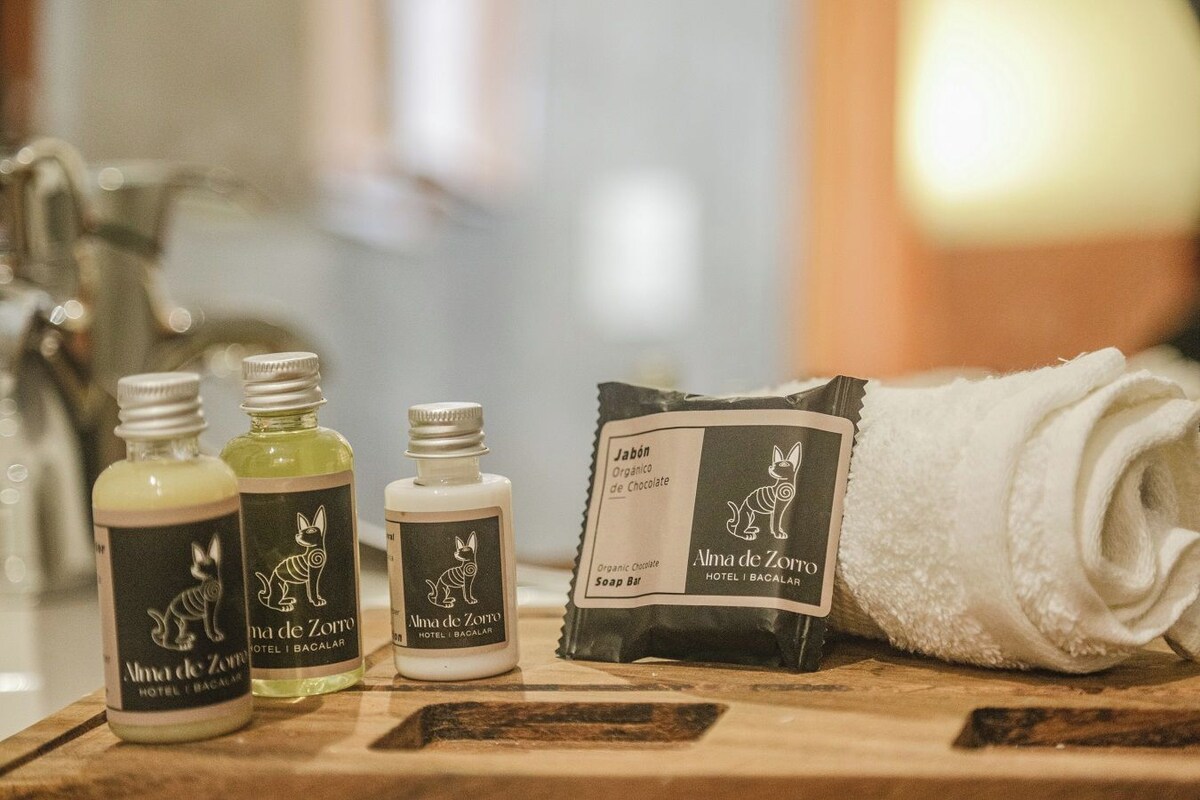 A wooden surface with three bottles of organic chocolate soap and a rolled white towel.