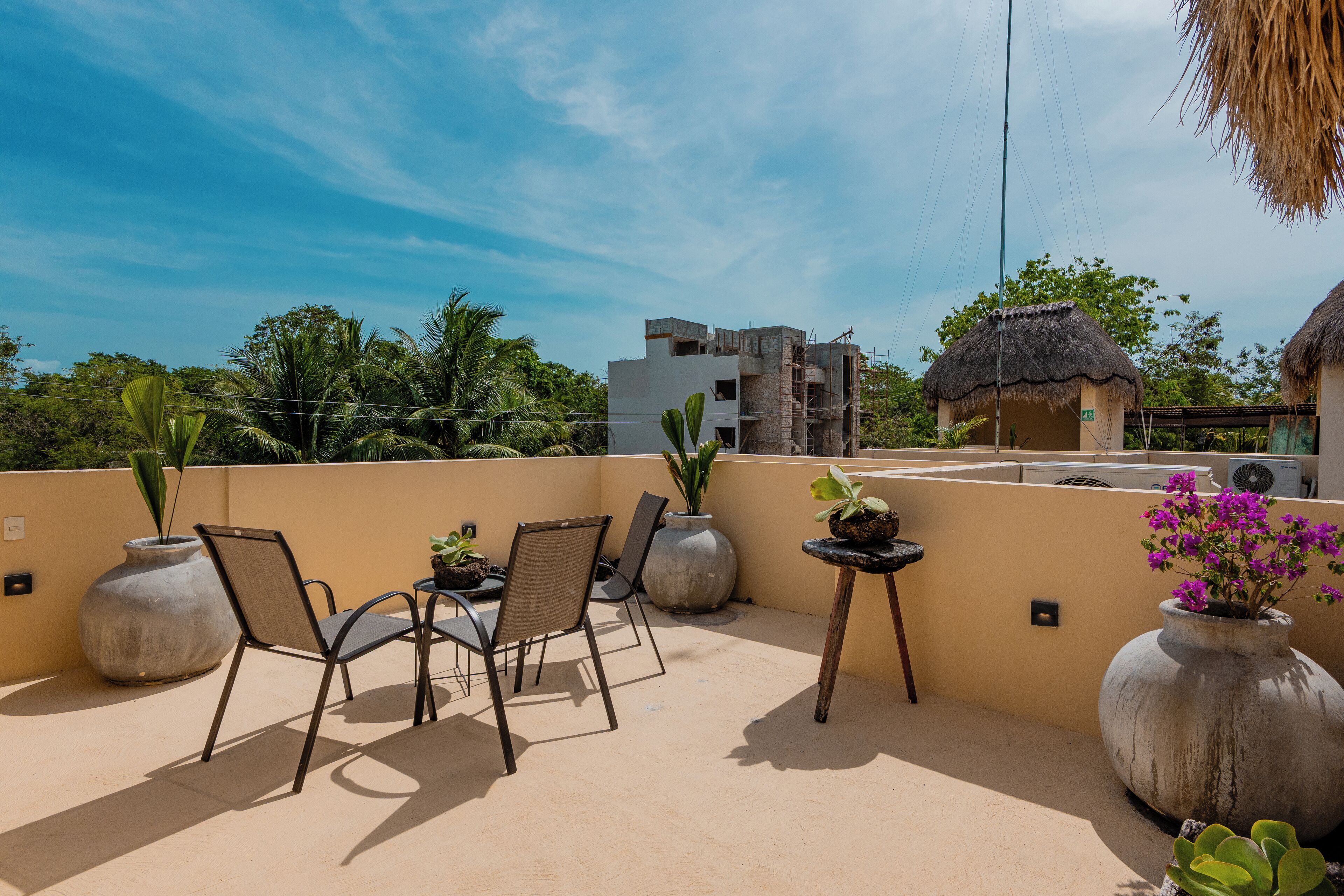 Una terraza en la azotea con cuatro sillas, dos jarrones grandes y una pequeña mesa.