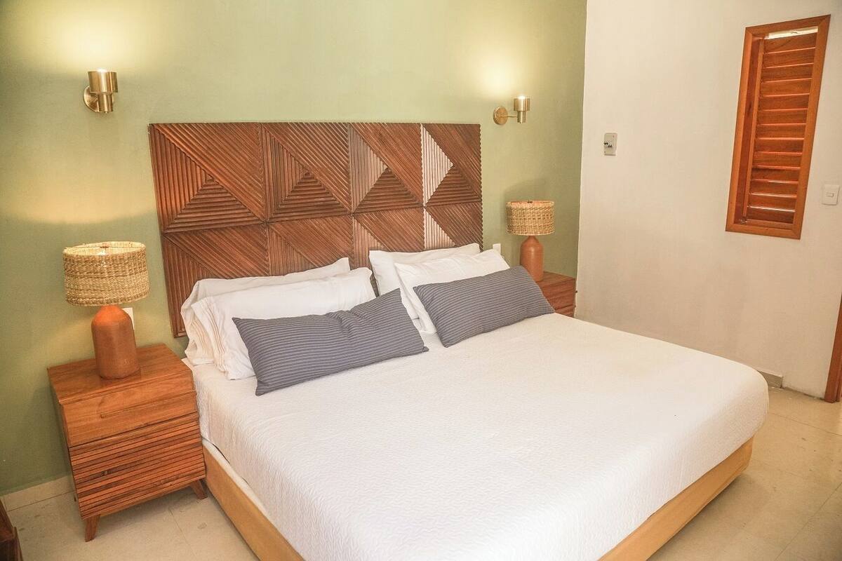 A bed with a geometric-patterned headboard, two bedside tables with lamps, and a door with wooden shutters.