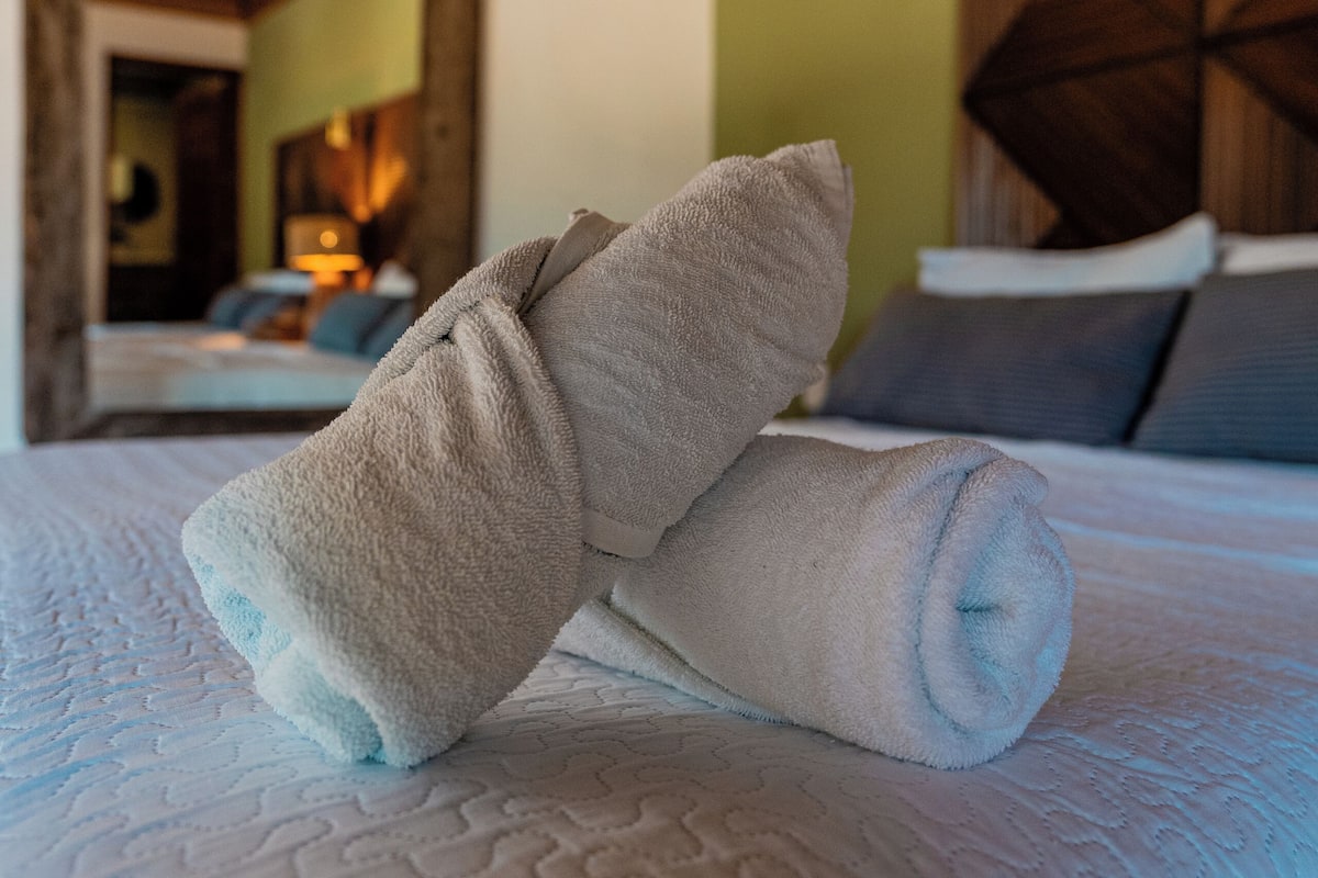 A neatly made bed with rolled towels, a wooden ceiling, and a geometric wall panel.