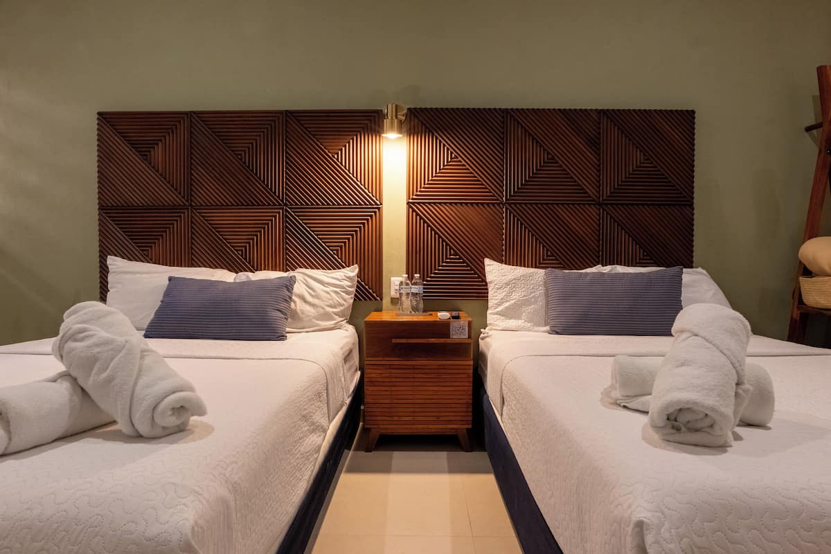A hotel room with two beds, a wooden headboard, a nightstand, and a chair.