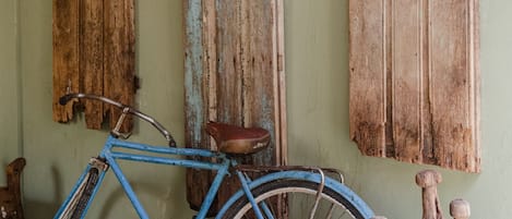 Una bicicleta azul apoyada en una pared con tres puertas de madera envejecida, una con marco azul y otra con huellas rojas.
