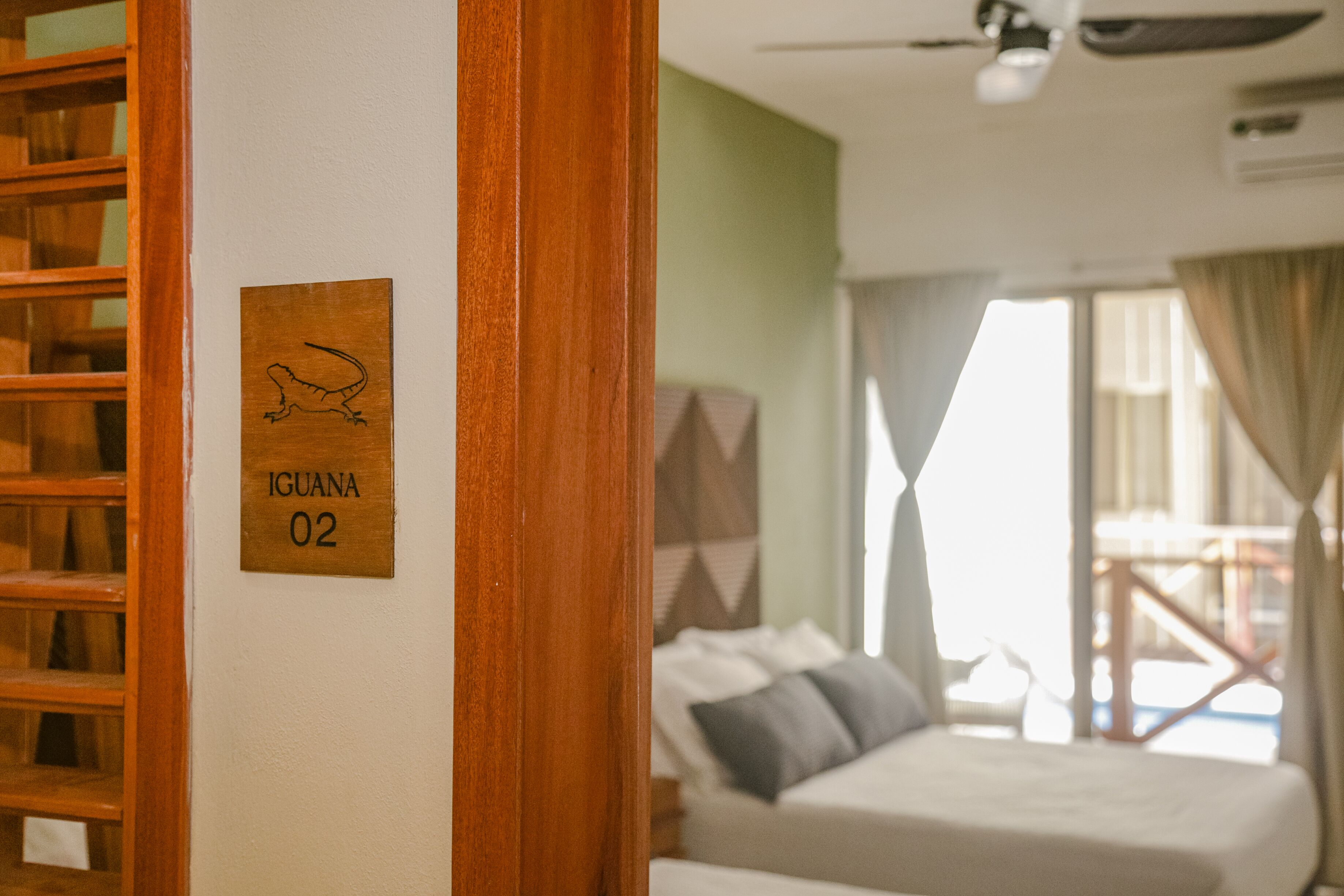 A hotel room with a bed, a wooden door frame, and a wall-mounted sign with a lizard and the text "IGUANA 02".