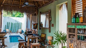 A rustic room with a thatched roof, a pool, and a wooden cabinet labeled "Coffee Station." - Alma de Zorro (Bacalar)