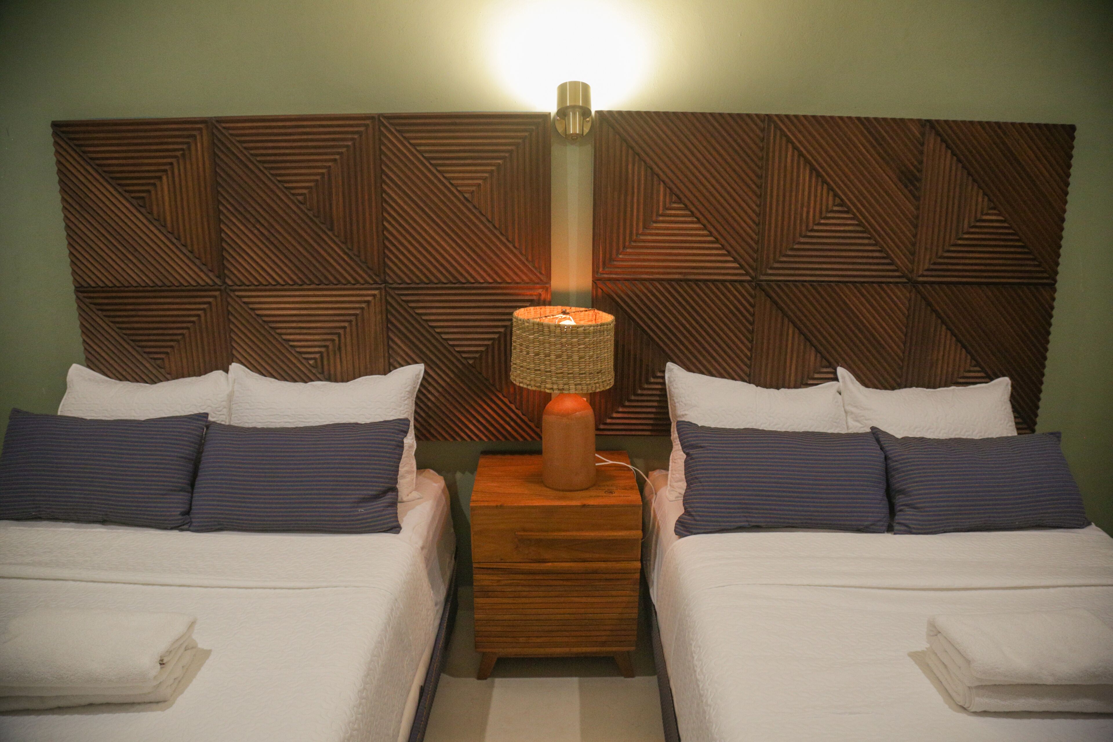 Une chambre d’hôtel avec deux lits, une tête de lit en bois et une table de chevet avec une lampe.