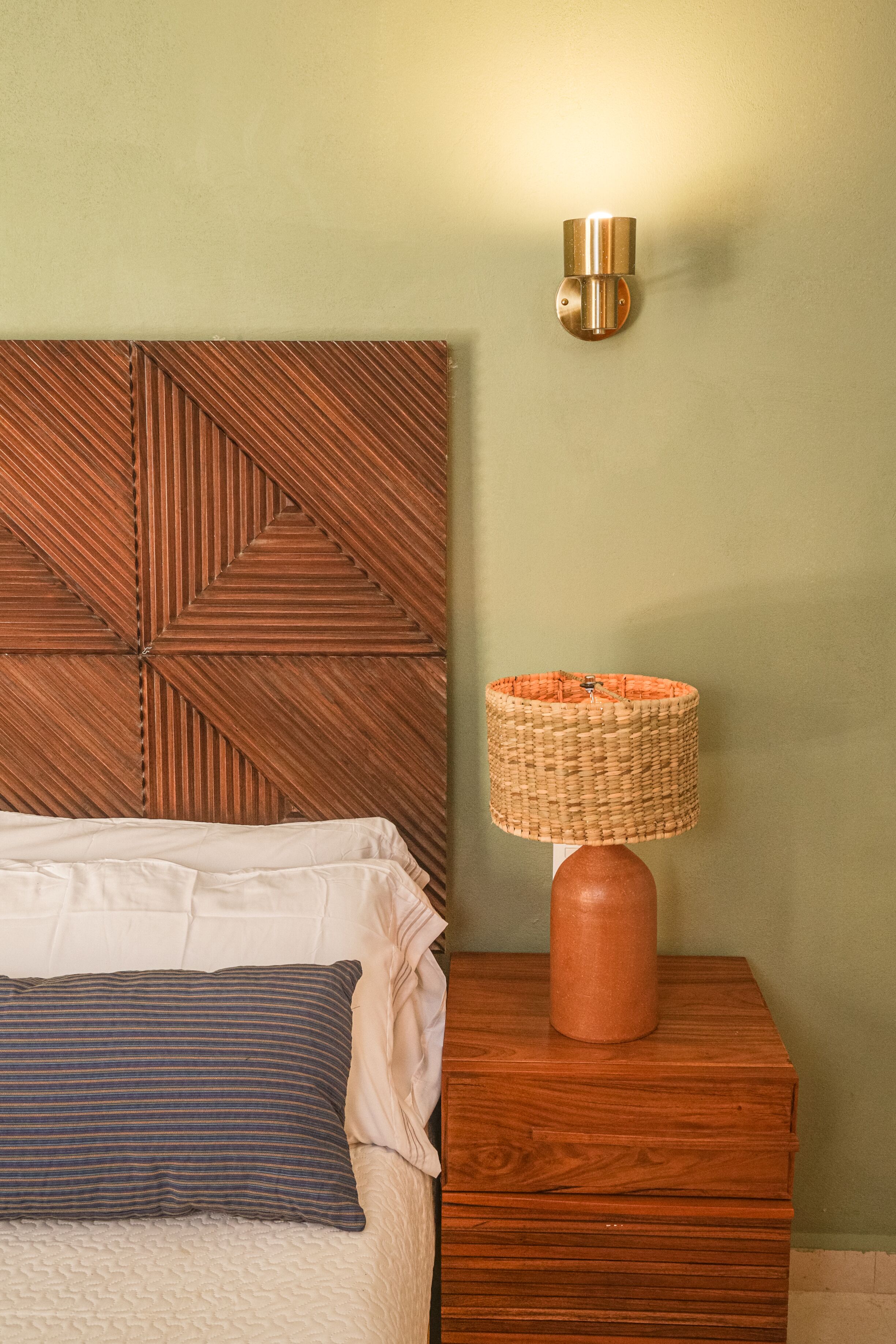 A bed with a wooden headboard, a bedside lamp, and a wall-mounted light fixture.