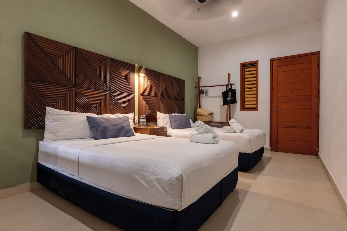 A hotel room with a large bed, a smaller bed, a wooden headboard, a nightstand, a lamp, a wardrobe, and a door.