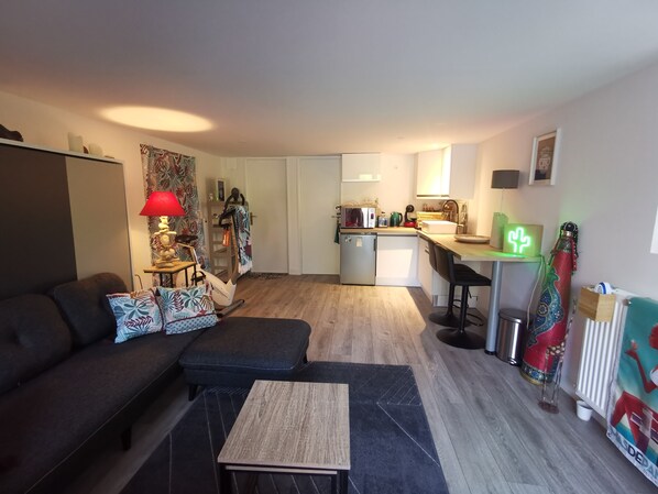 Un espace de vie compact comprenant un canapé, une petite table basse, un coin cuisine et un espace repas.