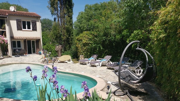 Ein Pool mit Liegestühlen und einer Hängematte, umgeben von Grünpflanzen und einem Haus.