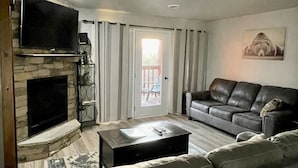 Un salon avec une cheminée en pierre, un téléviseur à écran plat, un canapé en cuir et une table basse.
