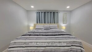 Una cama bien hecha con ropa de cama a rayas, un cabecero, dos lámparas de noche y una ventana con cortinas.
