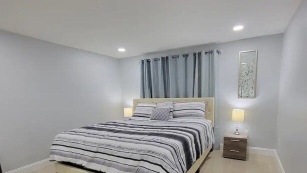Un dormitorio con cama, mesita de noche, lámpara y una obra de arte colgada en la pared.
