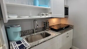 Una cocina con encimera de granito, pileta de acero inoxidable y armarios blancos.