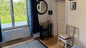 Une pièce avec une grande fenêtre, un miroir, une petite table avec une lampe, une chaise et un tapis à motifs.