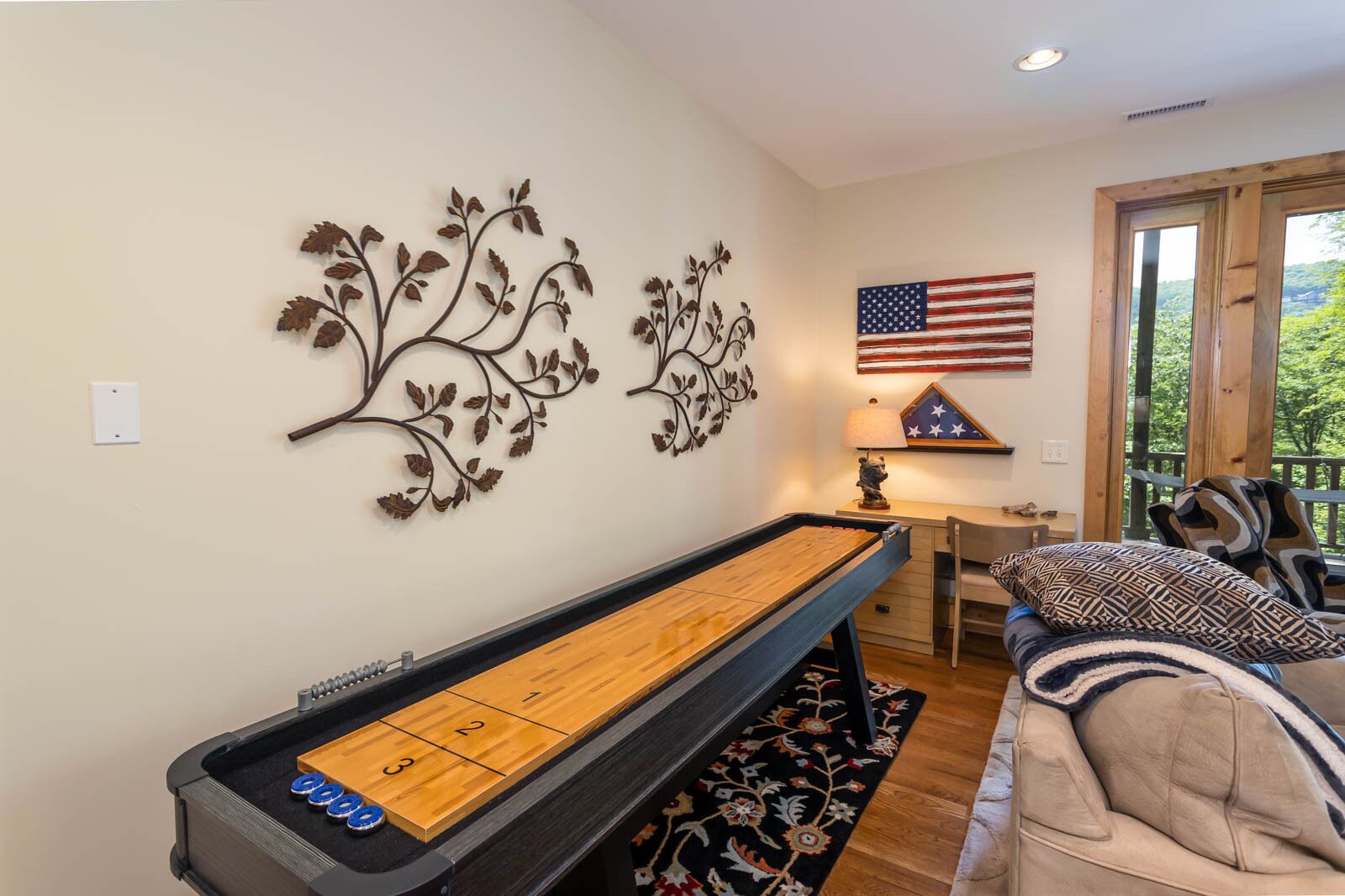 A room with a shuffleboard table, a couch, a lamp, and an American flag on the wall.
