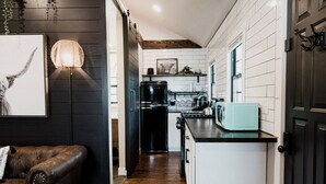 Uma cozinha moderna com azulejos brancos, uma geladeira preta, um micro-ondas verde-água e uma luminária pendente.