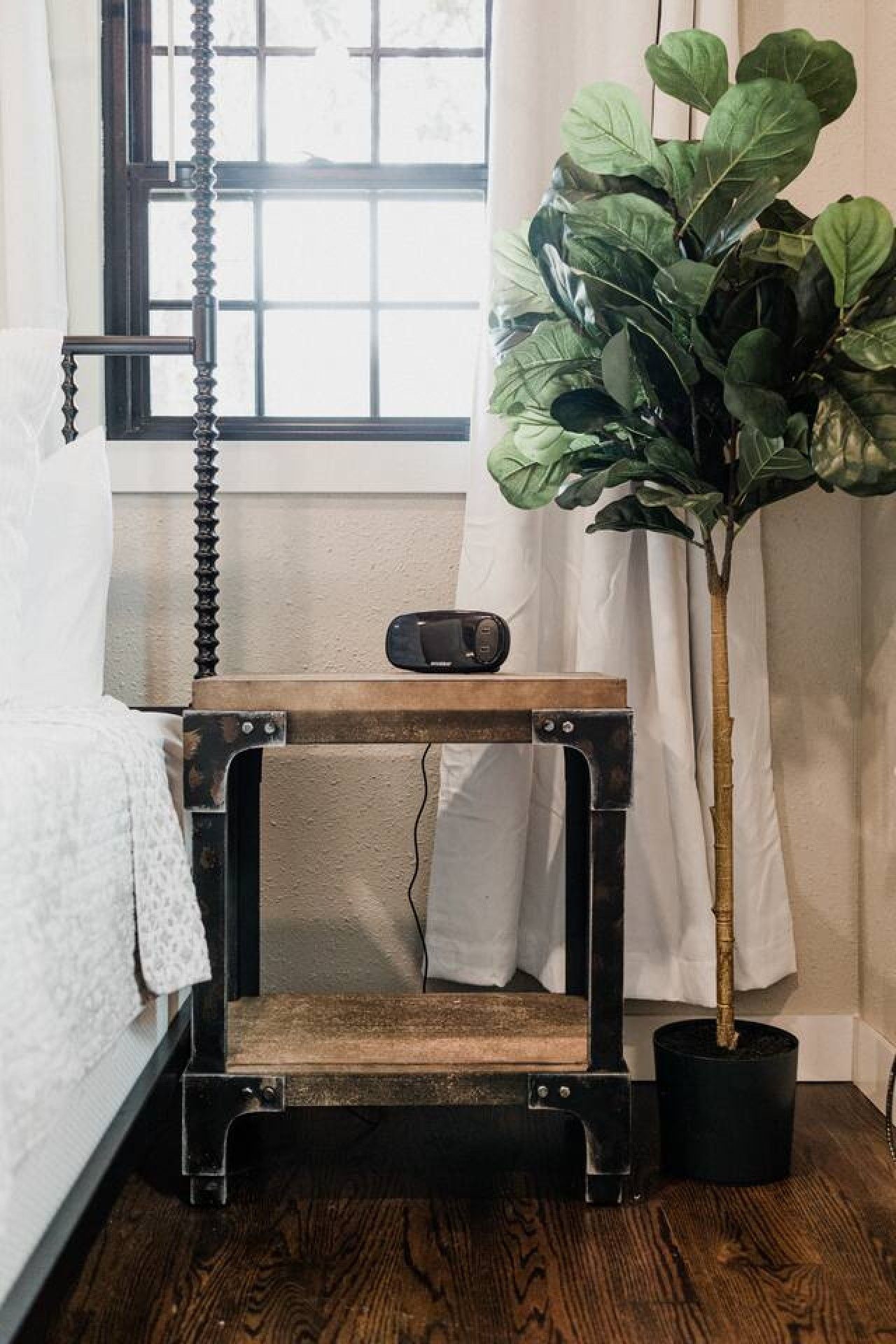 A room with a bed, a wooden cat tree, a potted plant, and a window with curtains.