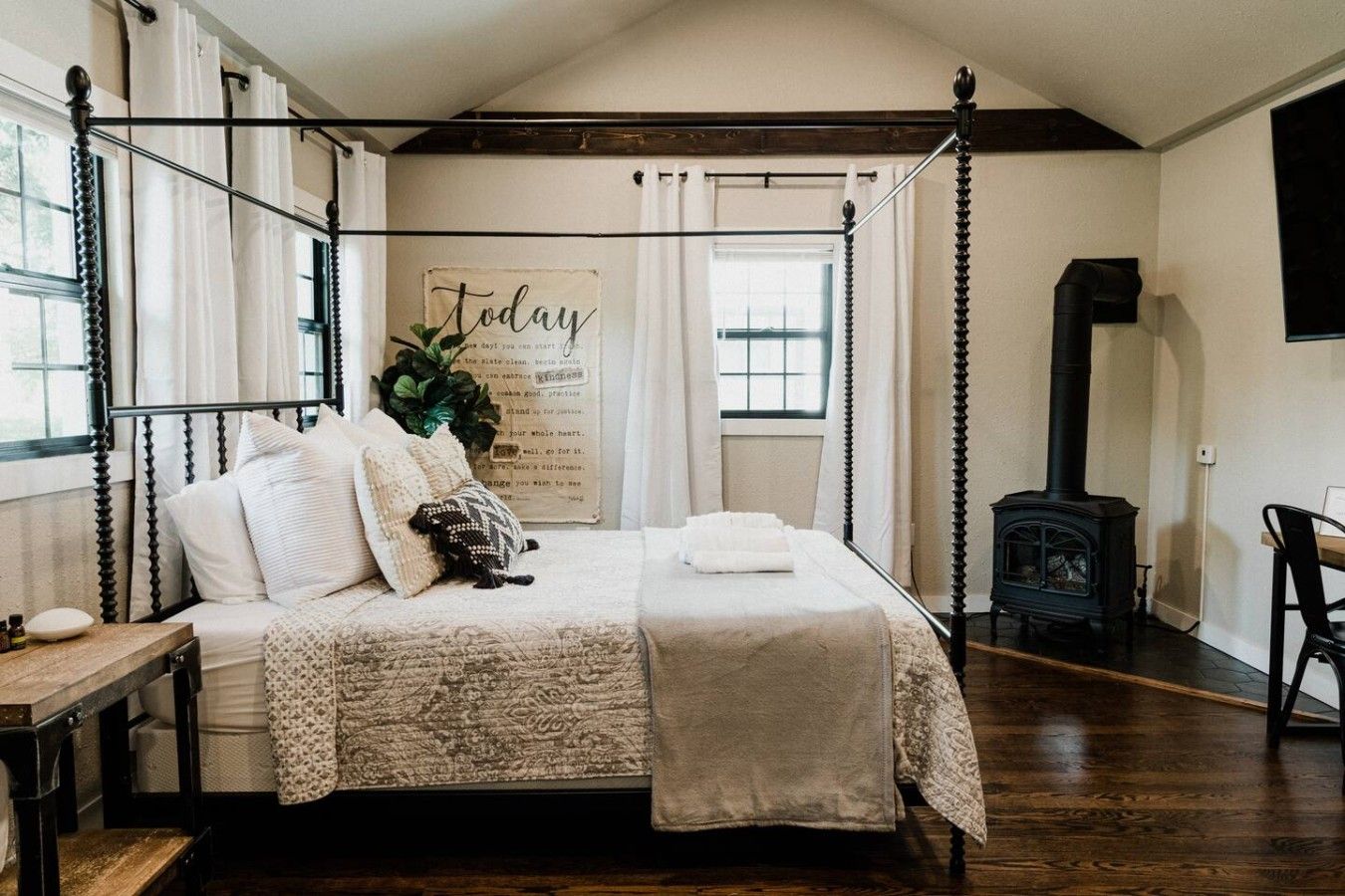 Un lit à baldaquin avec une tête de lit décorative, une table de chevet, un radiateur fixé au mur et une fenêtre avec des rideaux.