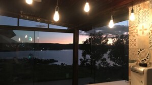 A modern room with large windows, a kitchen area, and hanging light fixtures. - Chalé Mirante Reservations only through the website ChalesTemporada.com (Alexânia)