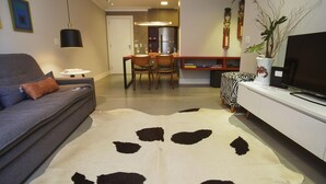 A living room with a grey sofa, a white coffee table, a cowhide rug, a zebra-patterned ottoman, a flat-screen TV, and a dining area with chairs and a table. - Modern in Ipanema Great for Families Re406 Z2 (Rio de Janeiro)