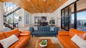 Un vaste espace de vie doté d’un plafond en bois, d’un ensemble de canapés, d’une table basse et d’un escalier menant à un niveau supérieur.