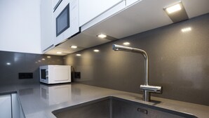 Une cuisine moderne dotée d’un évier en acier inoxydable, d’un four à micro-ondes et d’un éclairage sous les meubles hauts.