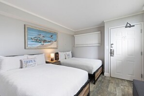 A bedroom with two beds, a painting of birds on the wall, a door, and a window with blinds.