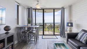 A modern living room with a balcony, a ceiling fan, and a view of the ocean.