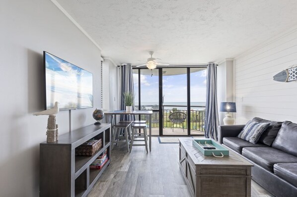 A modern living room with a balcony, a dining area, and a sofa. - Beachfront 1BR Condo in Myrtle Beach (Myrtle Beach)