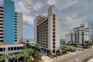 A multi-story hotel with a central courtyard, a parking lot, and a view of the ocean. - Beachfront 1BR Condo in Myrtle Beach (Myrtle Beach)