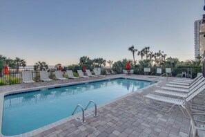 A swimming pool with lounge chairs and umbrellas, surrounded by palm trees and a fence. - Beachfront 1BR Condo in Myrtle Beach (Myrtle Beach)