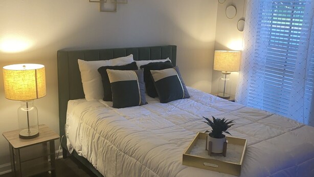 Une chambre à coucher bien rangée, avec un lit, deux tables de chevet dotées de lampes, un élément décoratif mural et une fenêtre avec des stores.