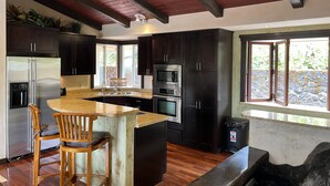 Een moderne keuken met donkere kastjes, een roestvrijstalen koelkast, een kookeiland met barstoelen en een plafondventilator.