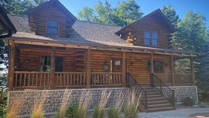 A log cabin with a stone foundation, a covered porch, and a staircase leading to the entrance.