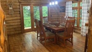 A rustic wooden dining room with a large table set for four, wooden chairs, and a deer head mounted on the wall.