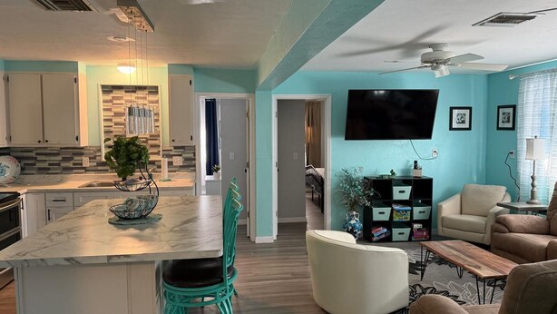 A modern kitchen with a marble countertop, teal chairs, and a dining area with a white sofa and a coffee table. - Weeki Wachee Gardens on the Canal (Spring Hill)