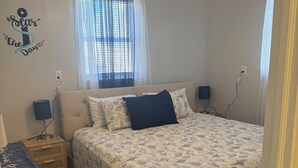 A bedroom with a bed, nightstands, a ceiling fan, and a window with curtains. - Weeki Wachee Gardens on the Canal (Spring Hill)