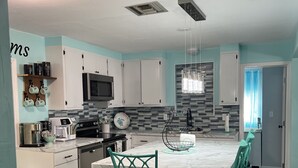 A modern kitchen with white cabinets, a central island with bar stools, a microwave, and a hanging light fixture. - Weeki Wachee Gardens on the Canal (Spring Hill)