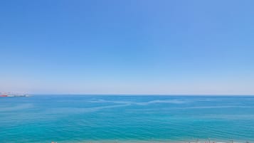 Una playa con cielo azul despejado, mar tranquilo y numerosos sombrillas de colores.